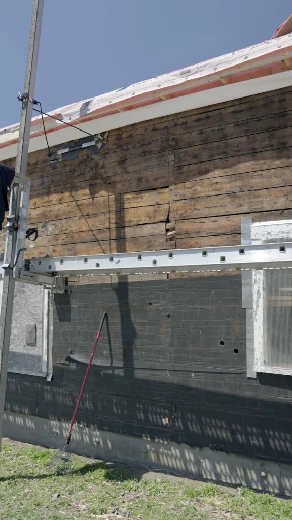 Pump-jack scaffolding against the barn wall with black weather barrier on the lower wall